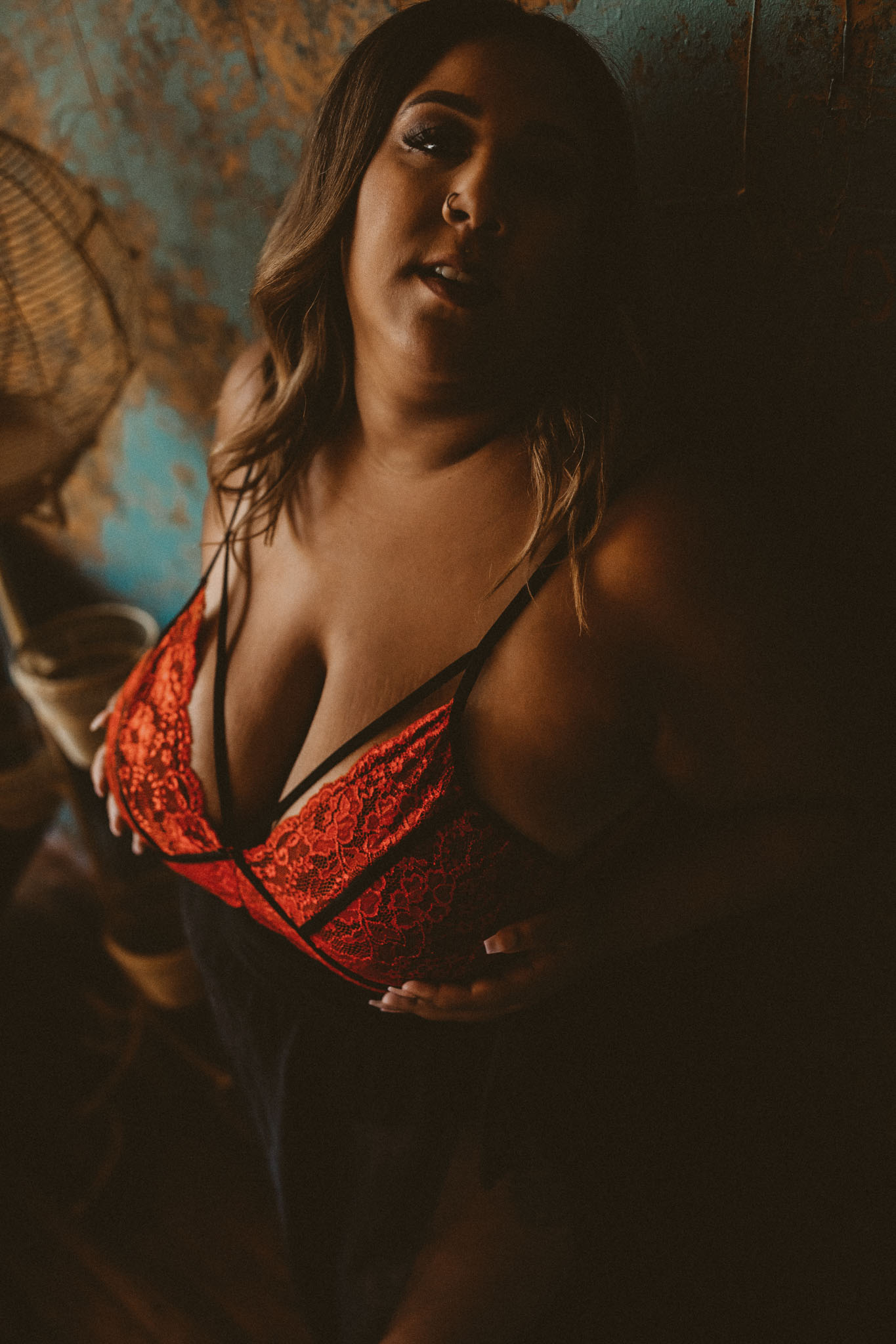Boudoir photo of a woman of color wearing red and black lingerie in a rustic bedroom at the J&S Photography studio in Shirley, Massachusetts
