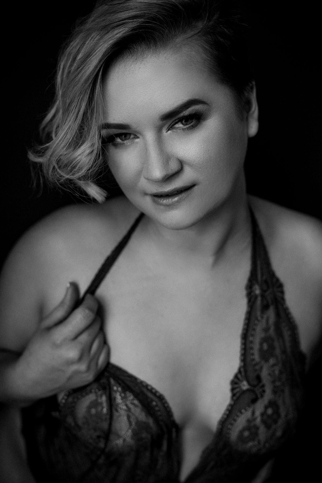 Jessie Clements holding the strap of her sheer black lace bodysuit and looking at the camera, photographed by Teri Hofford