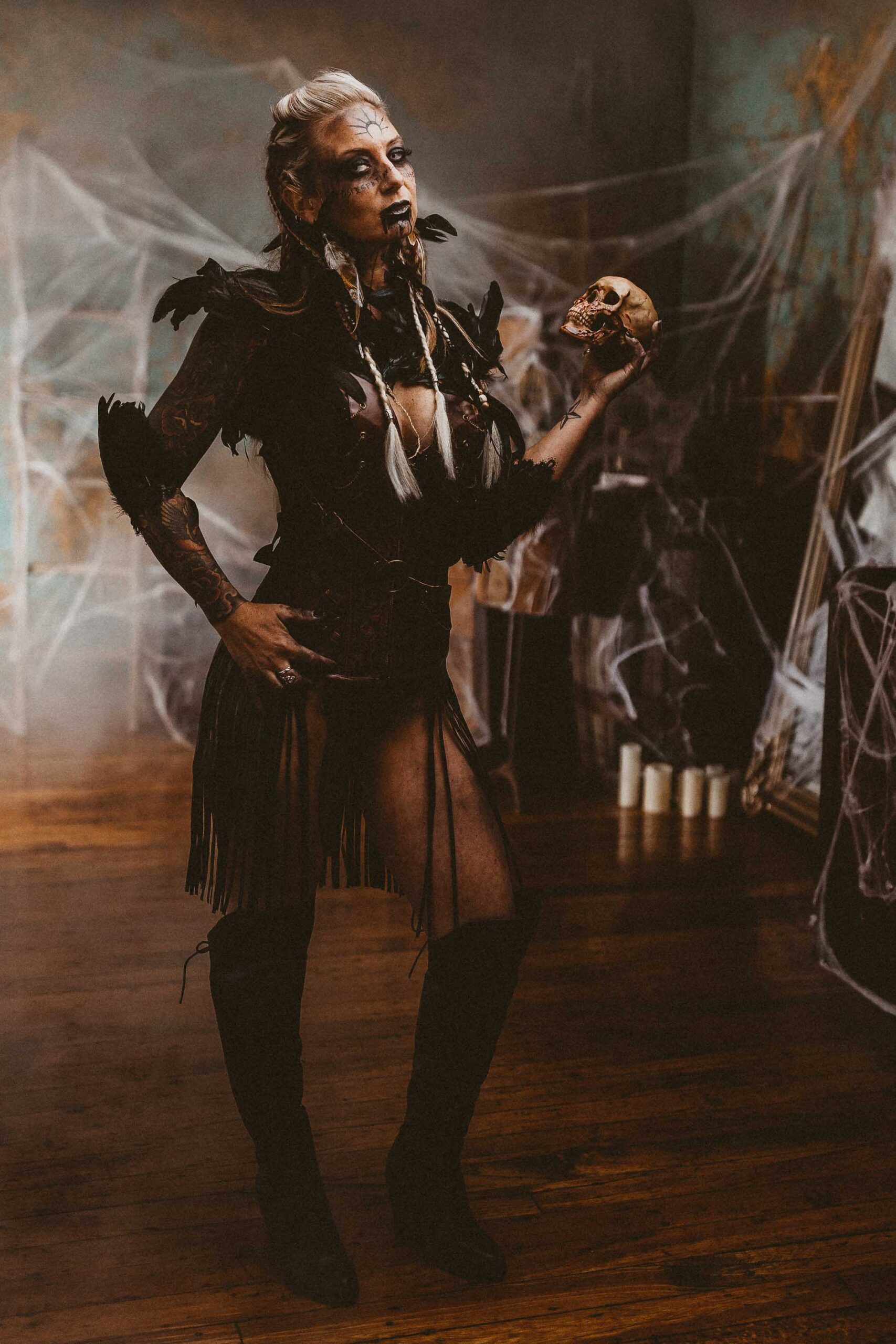 A blonde woman with black lipstick, viking style hair and makeup, and black boots and bodysuit holding a skull in the Boudoir by J&S Photography studio near Boston, Massachusetts